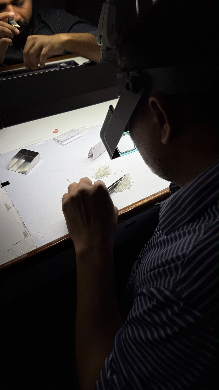 A grader sorting a parcel of loose diamonds under a head loupe at Sahyog Diamond